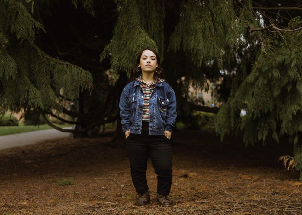 Person in denim jacket standing under trees.