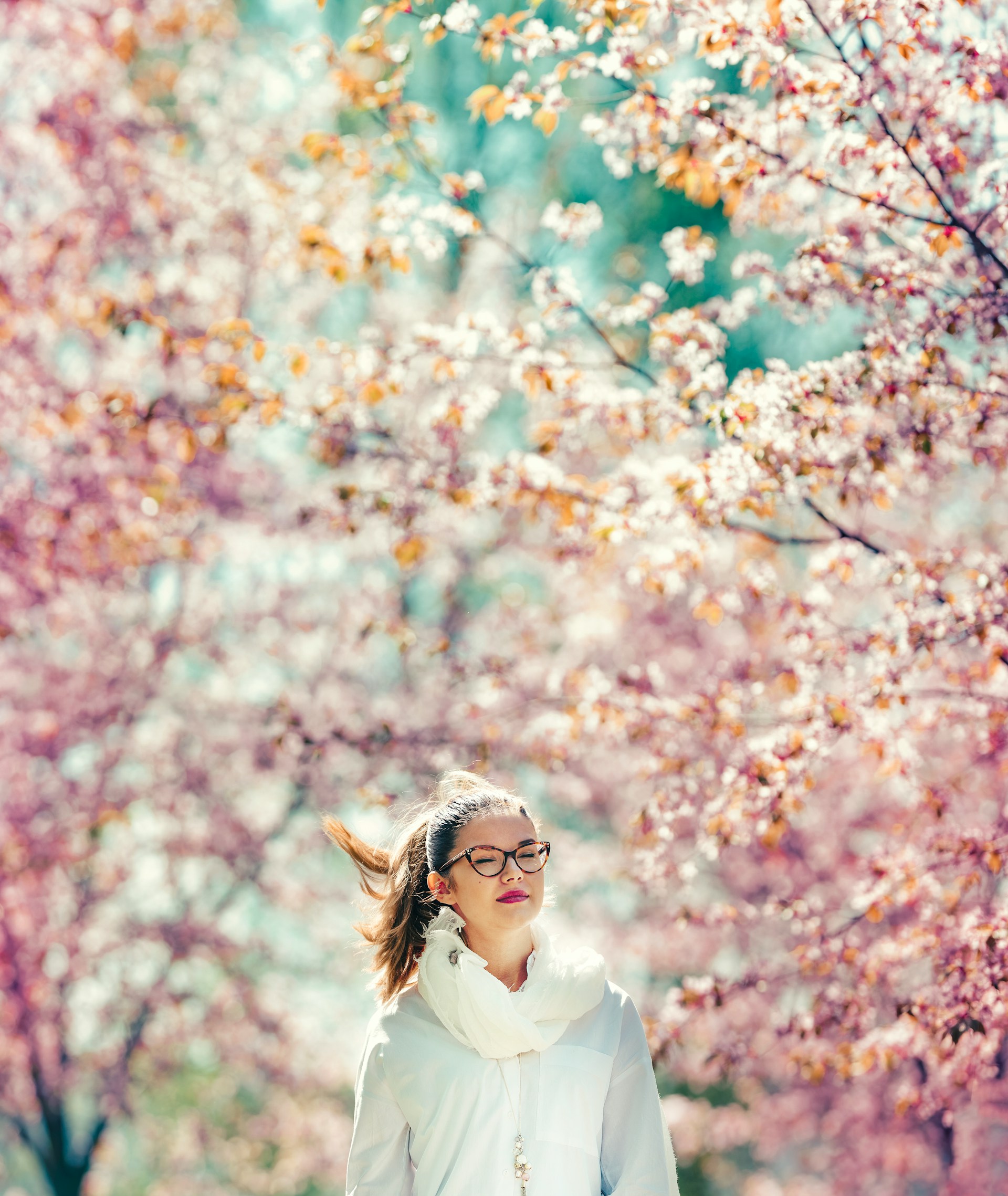 Woman stands peacefully under blooming pink cherry trees.