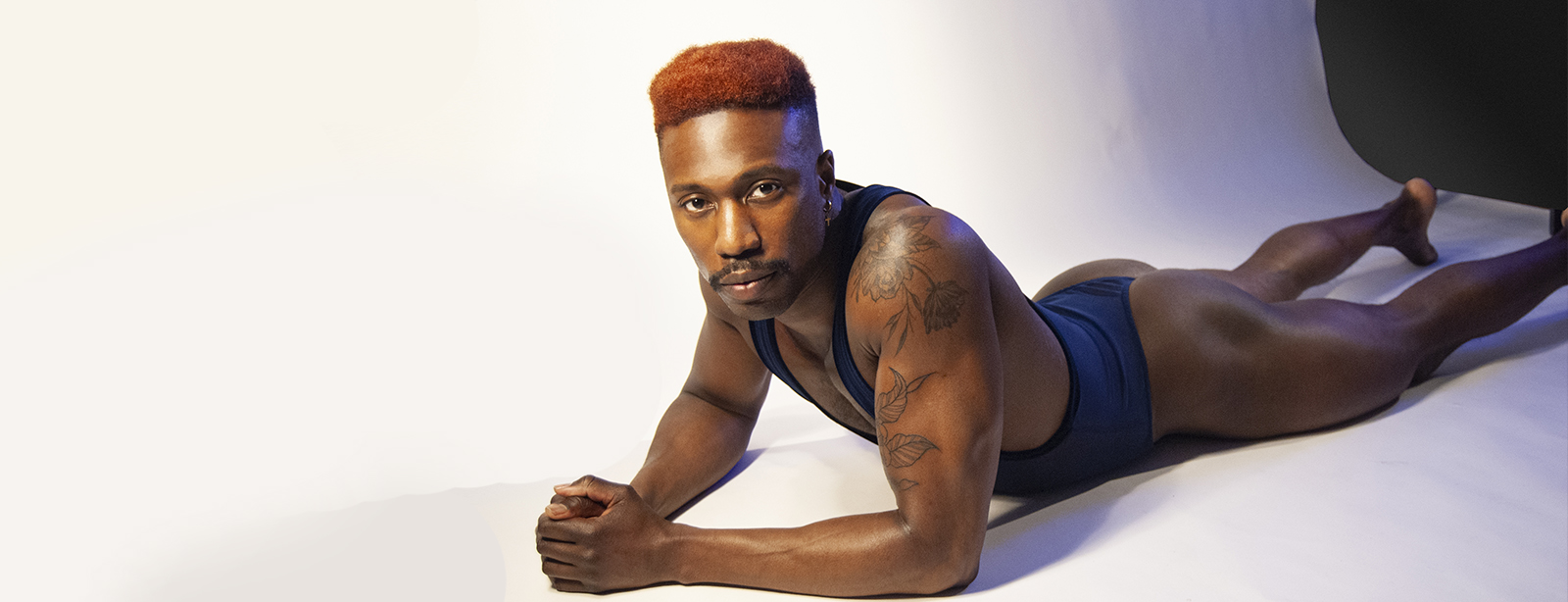 A dark-skinned person in a blue leotard lying on the floor.