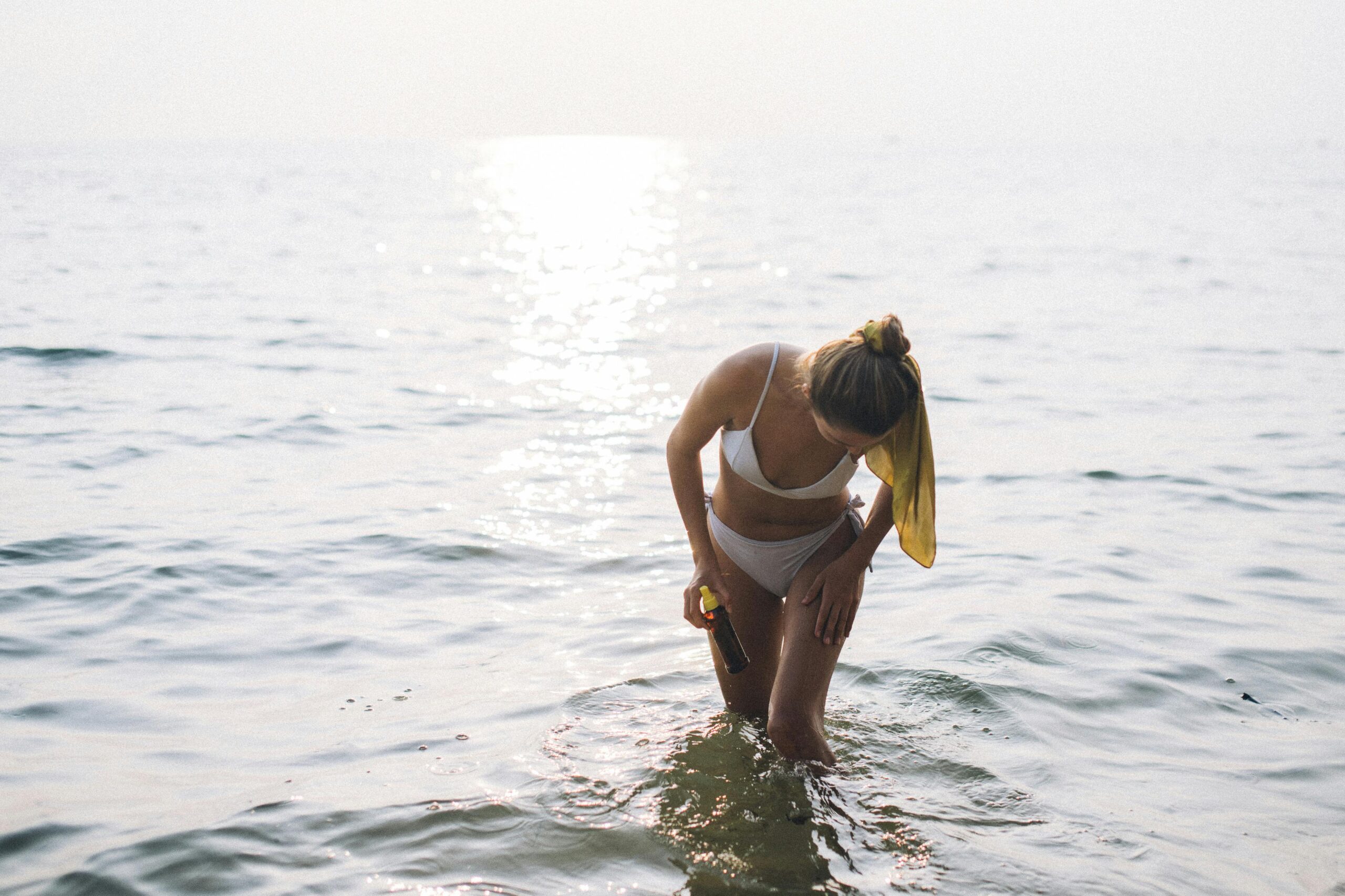 Woman in white bikini applying sunscreen in ocean.