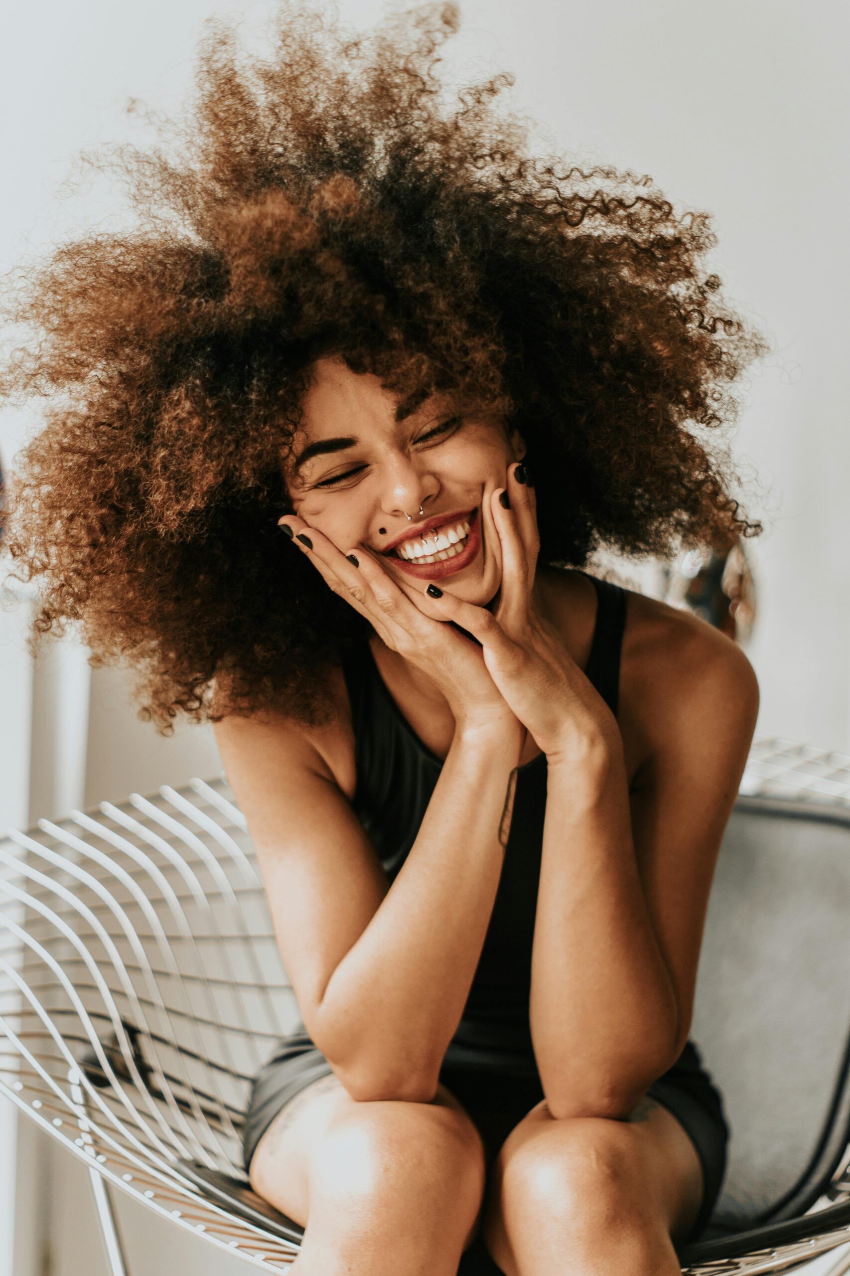 oyful woman with big curly hair sitting and laughing.