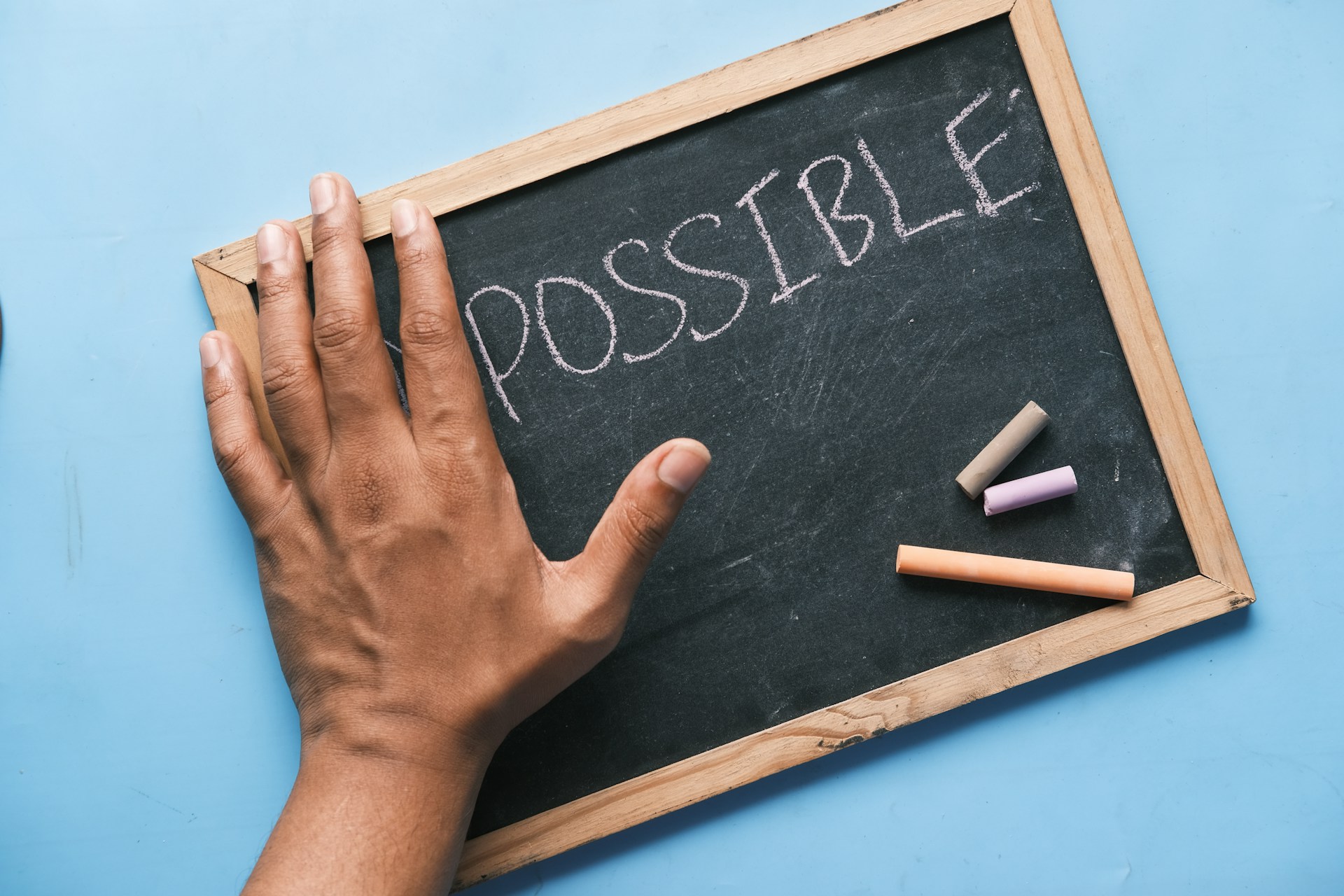 Hand reaches towards the word "possible" on a chalkboard.