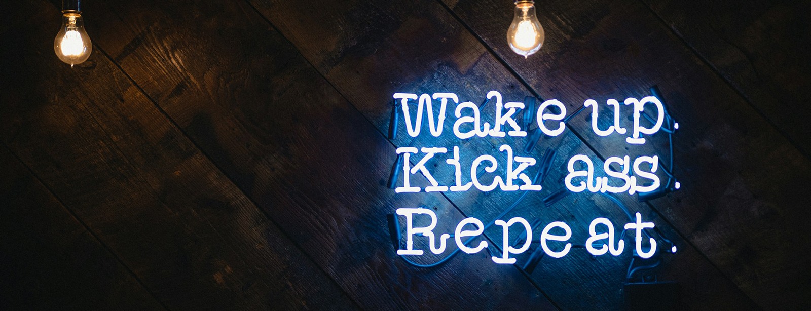 Blue neon sign: "Wake up. Kick ass. Repeat."
