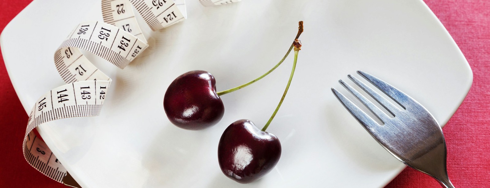 Cherries and tape measure on white plate for dieting.