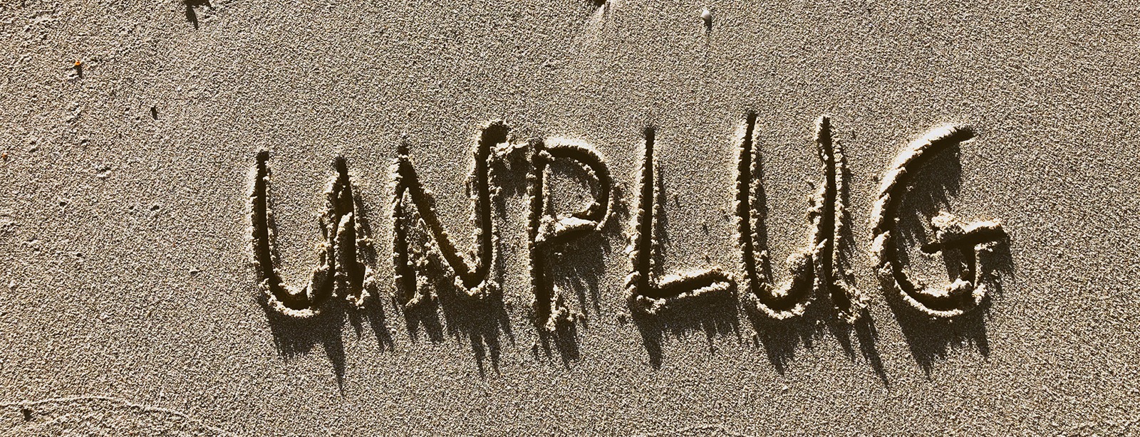 The word "UNPLUG" written in beach sand.