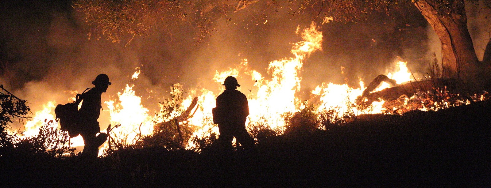 Firefighters silhouetted against a huge blaze.