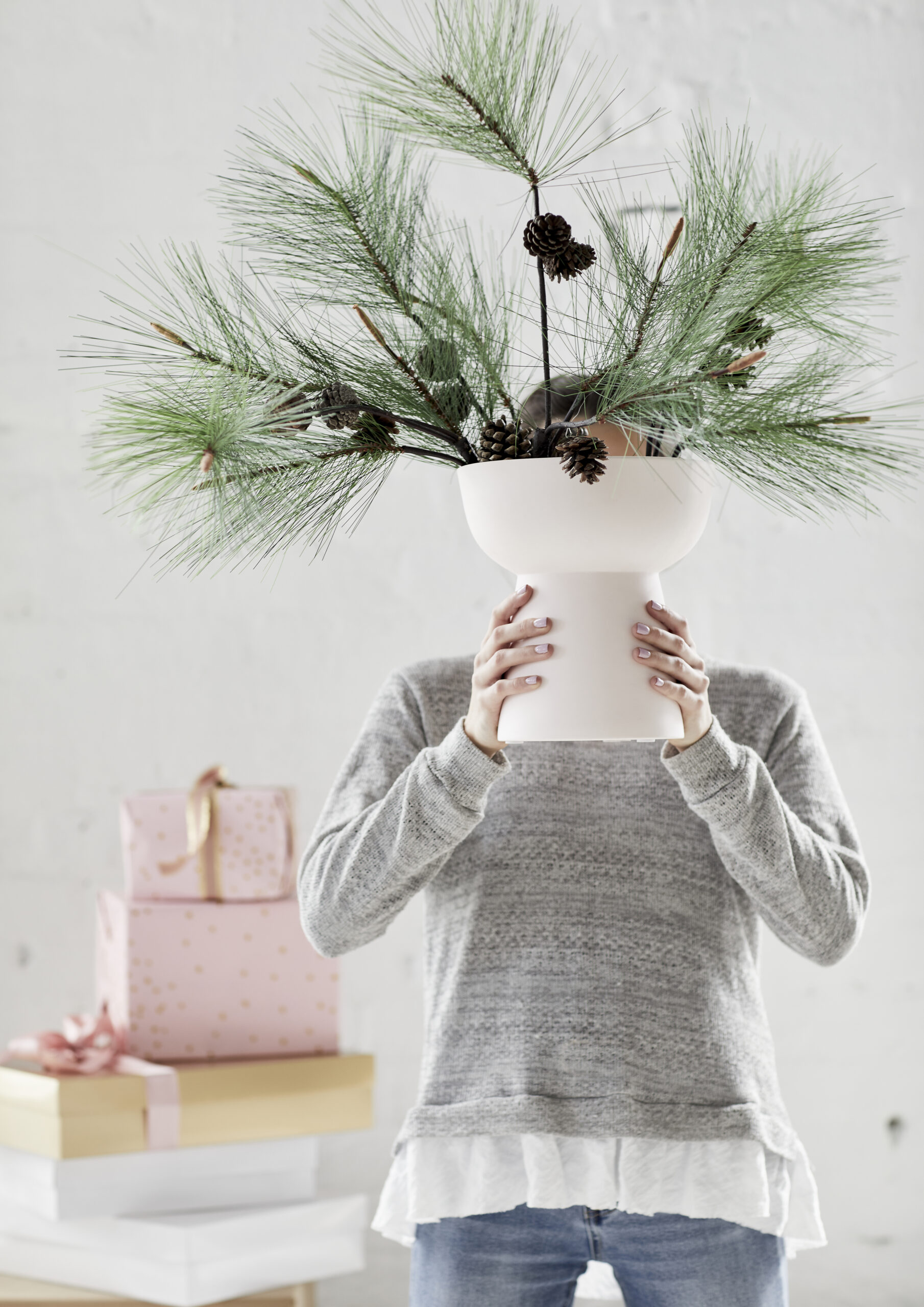 Person holding white vase with pine decorations.