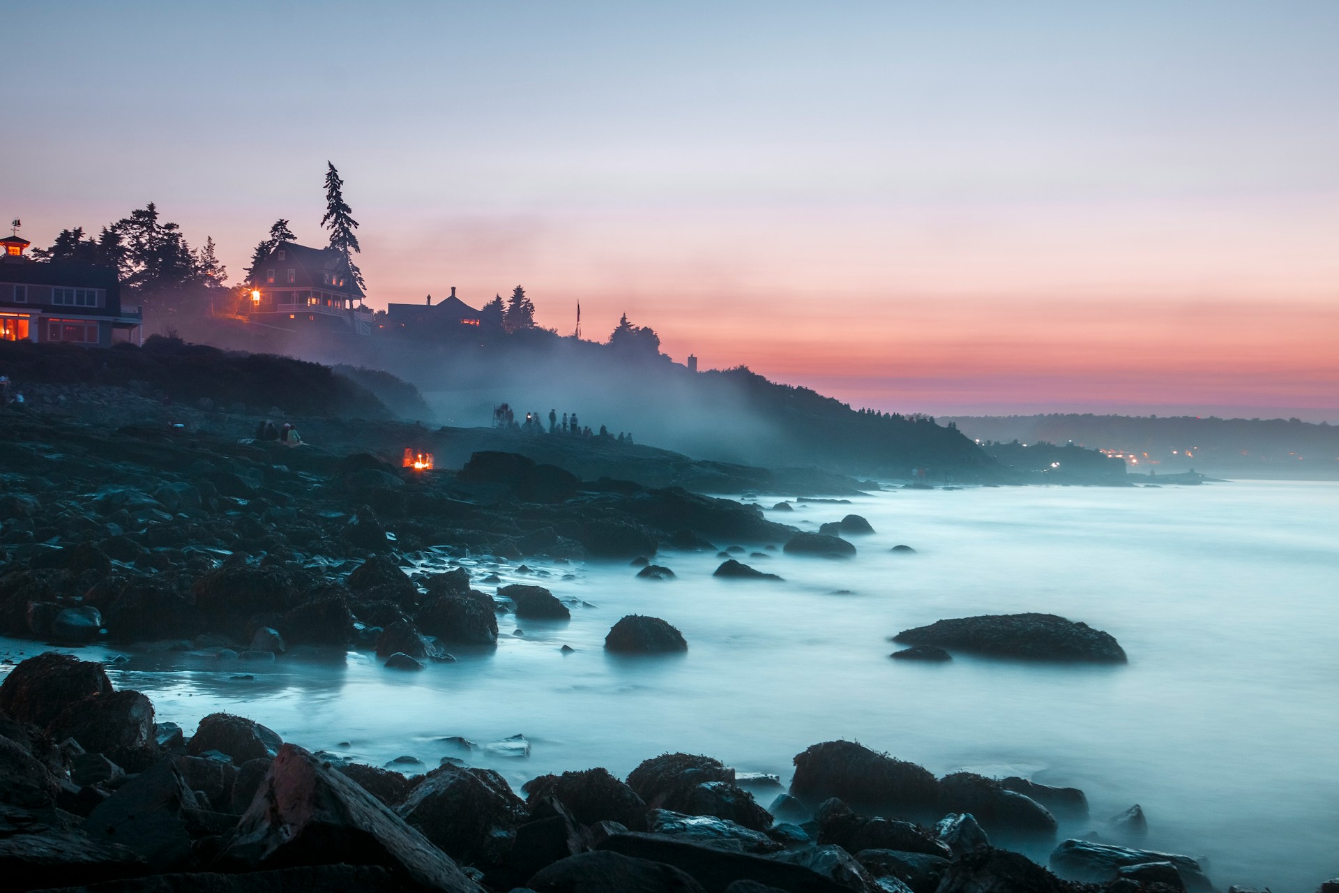 Rocky coastline with fog and lights at twilight.