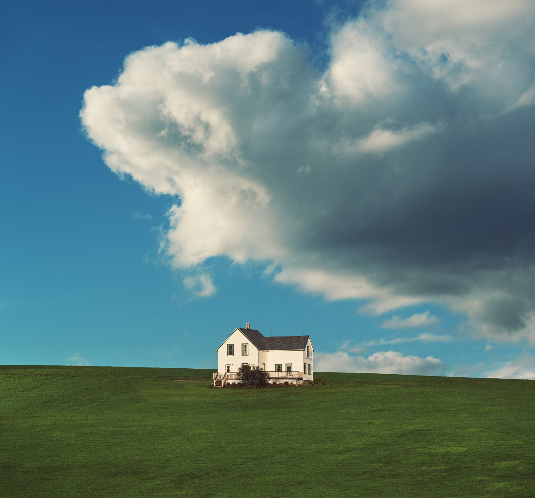 White farmhouse on green hill under massive cloud.