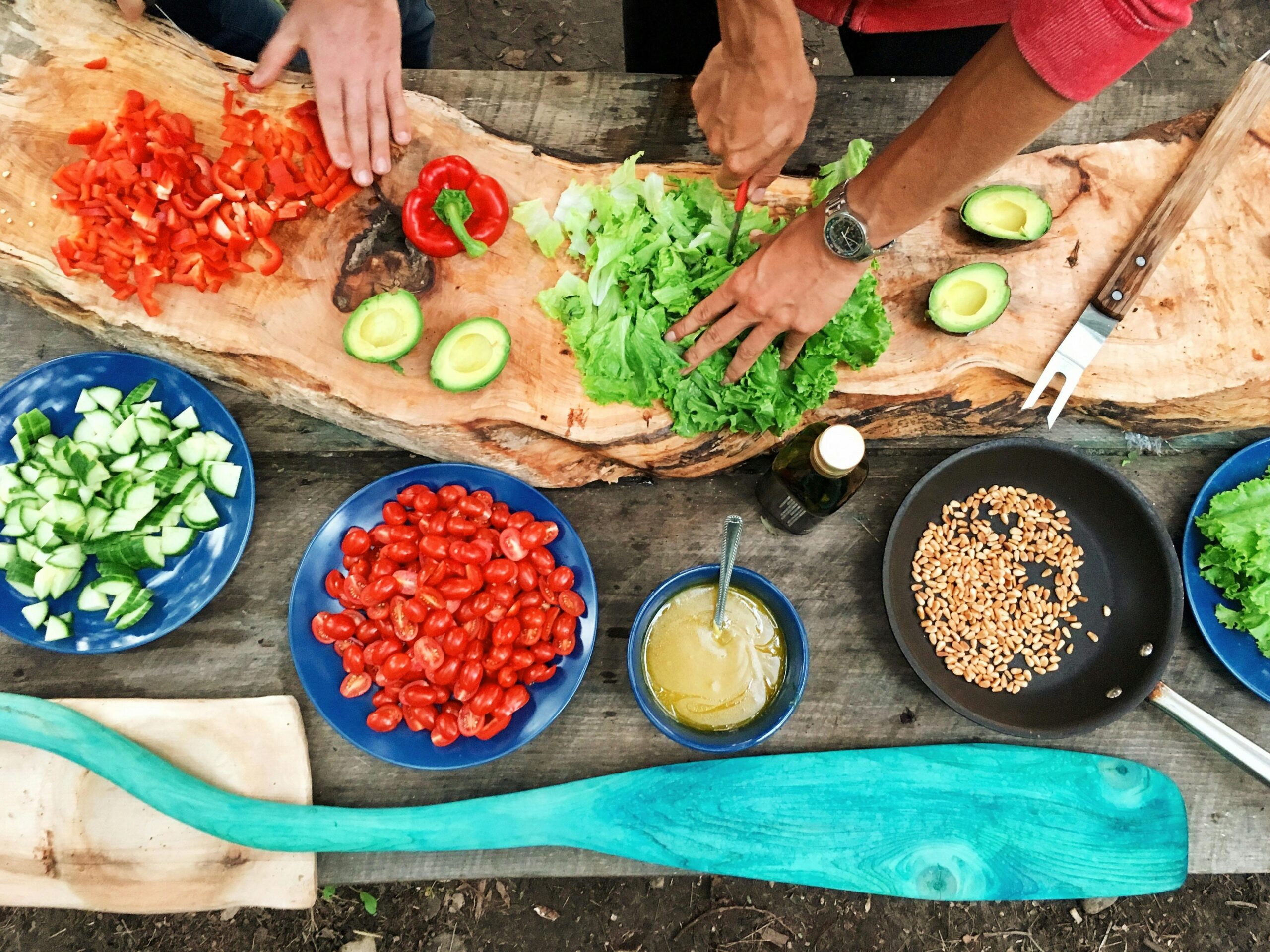 People chopping colorful fresh vegetables for a vegan meal.