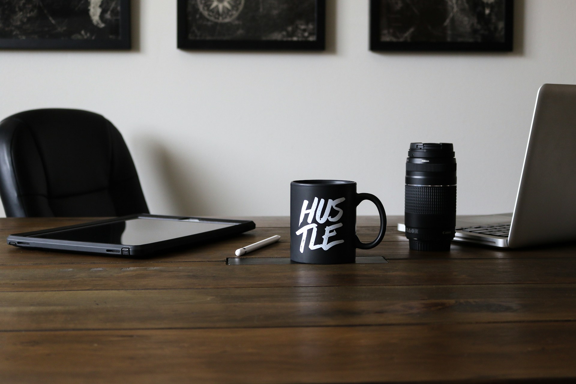 Desk with "Hustle" mug, laptop, and camera lens.