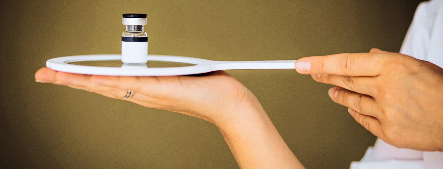 Hand holding small medical vial on white tool