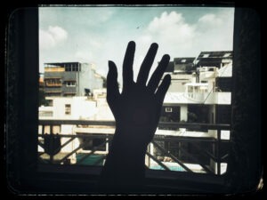 Silhouette of hand against cityscape by window