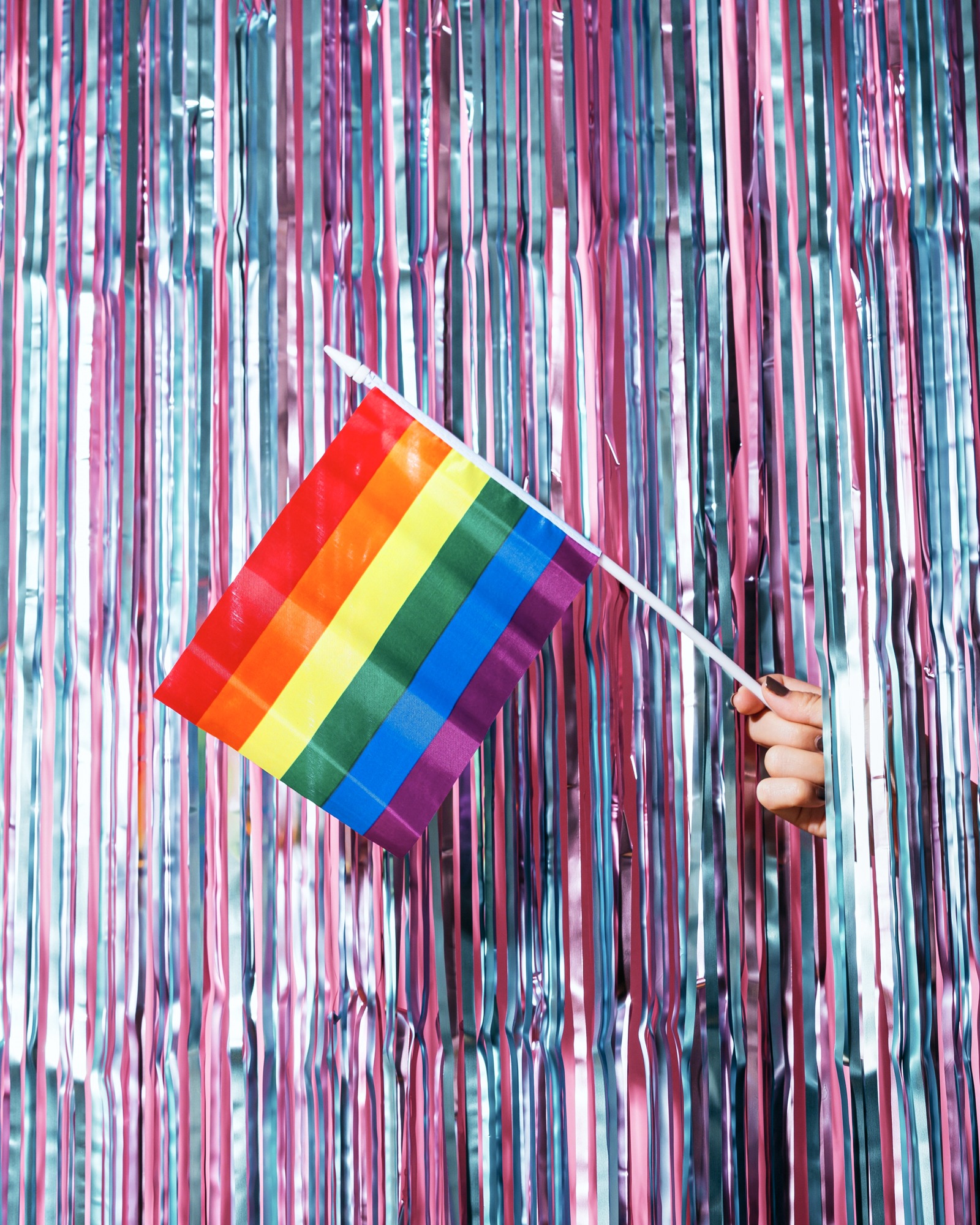 Hand holds rainbow flag by metallic streamers