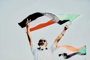 Man triumphantly holding Sudanese flag aloft outdoors