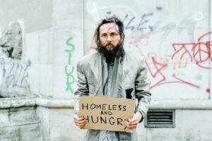 Bearded homeless man holding sign 'Homeless and Hungry'
