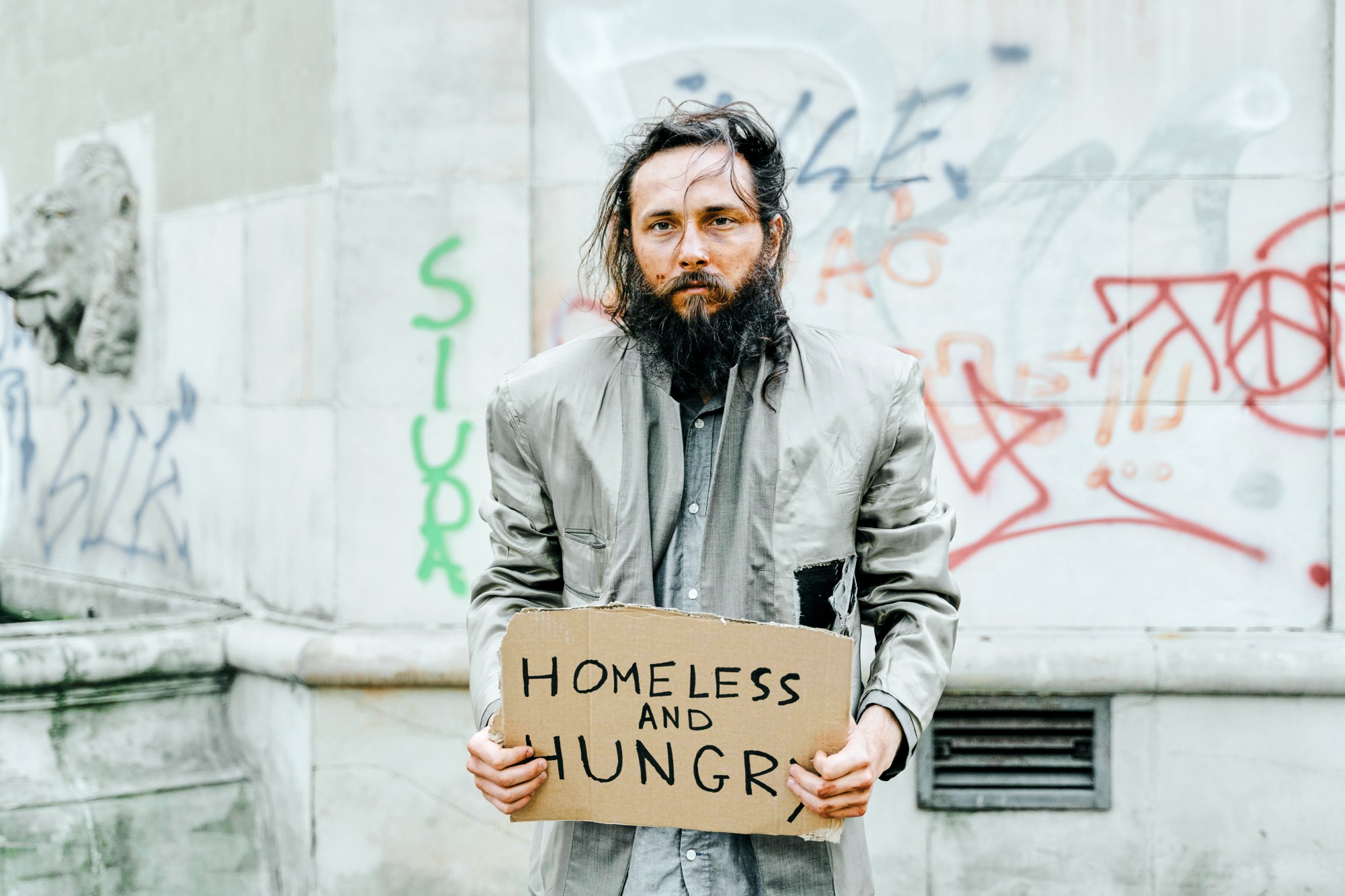 Bearded homeless man holding sign 'Homeless and Hungry'